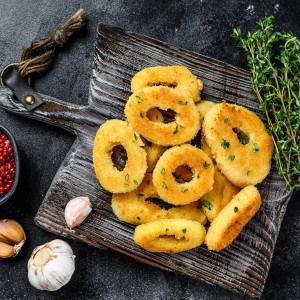 Deep fried squid calamari rings breaded on a cutting board. Black background. Top view