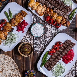 Flat lay Persian table with a mix of kebabs, traditional bread, and traditional Persian Carpet.